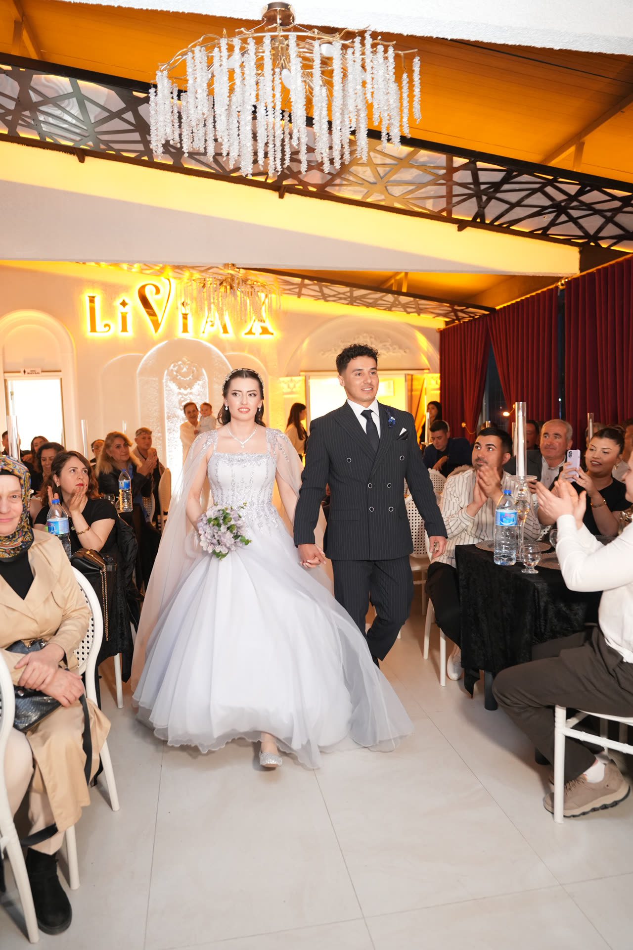 Gelin ve damat, kristal avizenin altında alkışlar arasında LiviaX salonuna giriyor
